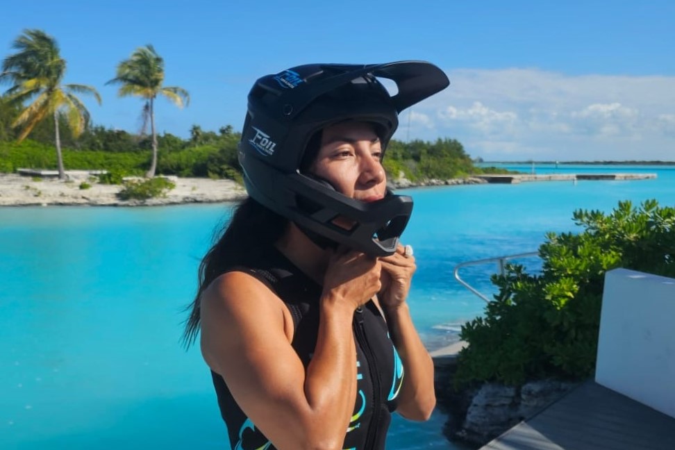 A female efoil rider preparing for safe foiling lesson putting on a full-wrap helmet.